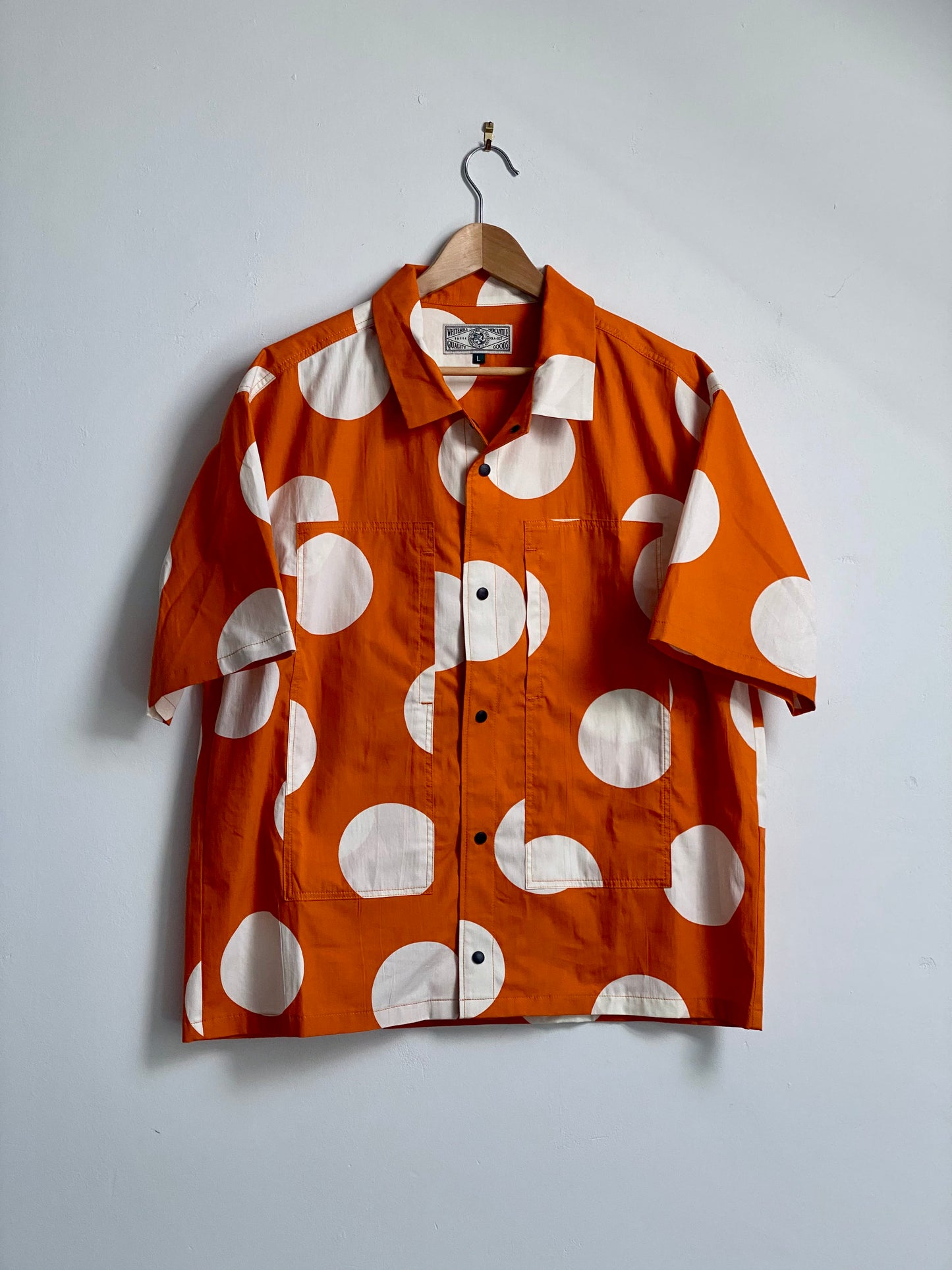 Orange short sleeve shirt with large white spots against a white background