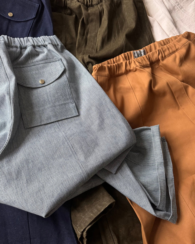 Stack of folded pants in various colors including gray, brown, and green.