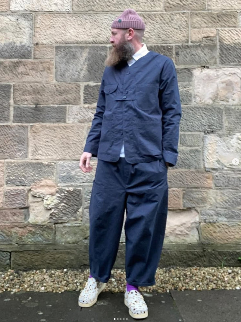 Man wearing a navy blue outfit standing against a stone wall.